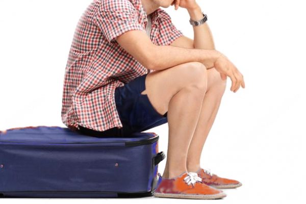 Man sitting on suitcase wearing shorts